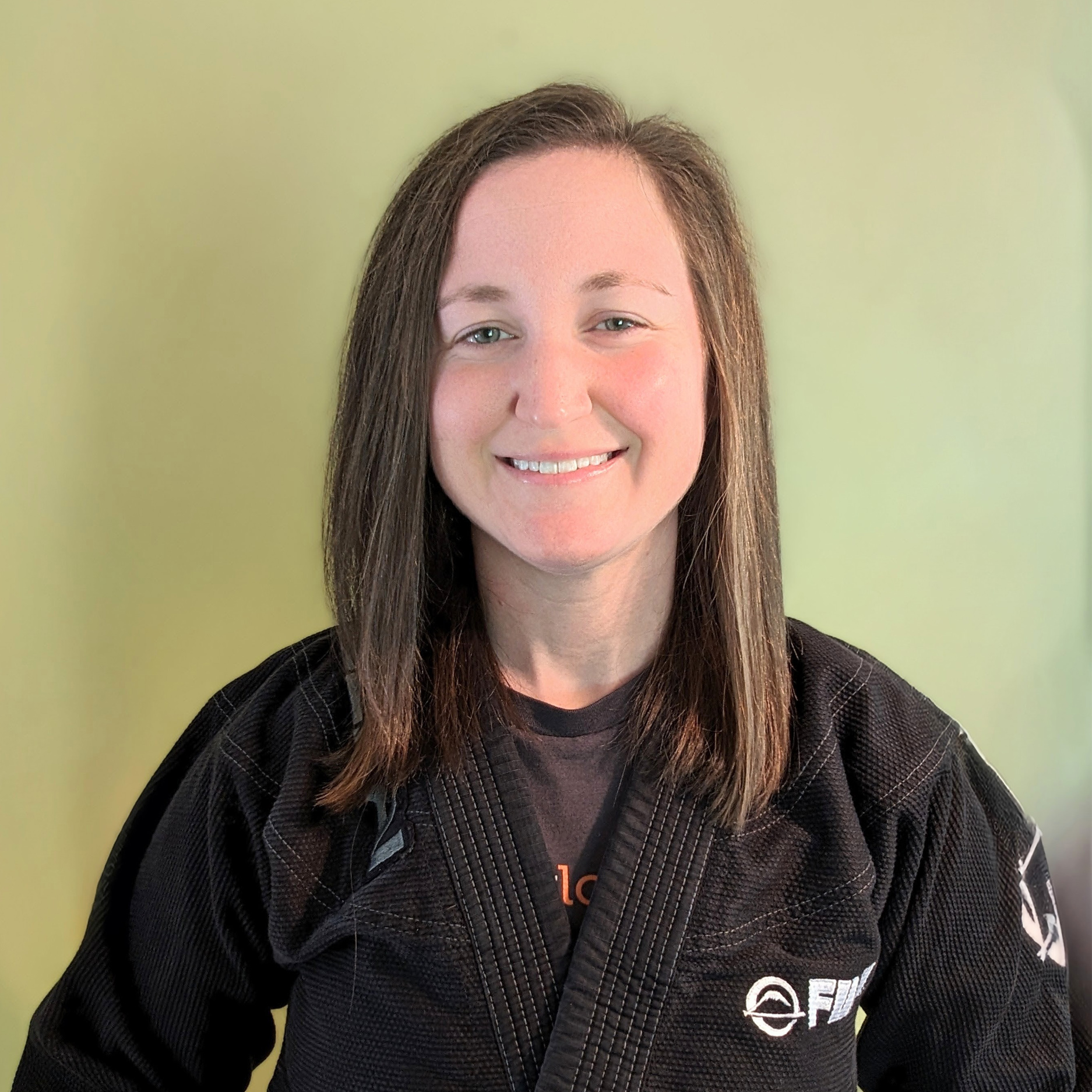 A smiling head-shot of Coach Lesley Steiner wearing a black gi. She has her hair down. It is shoulder length.